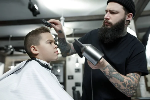 Coiffeur enfants coupant petit garçon sur un fond sombre . — Photo