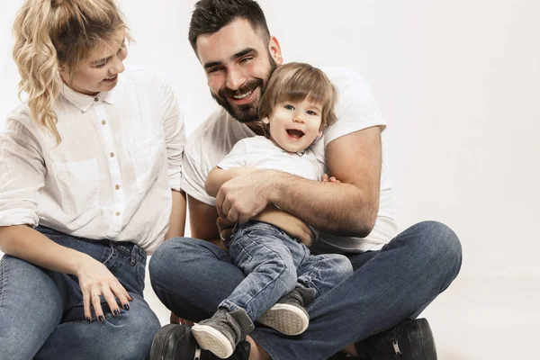 Família feliz com criança sentada junto e sorrindo para a câmera isolada no branco — Fotografia de Stock