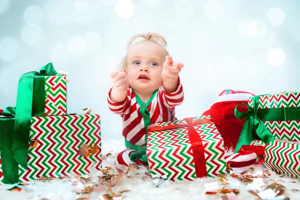 Χαριτωμένο μωρό κορίτσι 1 χρονών κοντά σε santa καπέλο ποζάρει πάνω από Χριστούγεννα φόντο. Κάθεται στο πάτωμα με Χριστουγεννιάτικη μπάλα. Περίοδος διακοπών. — Φωτογραφία Αρχείου