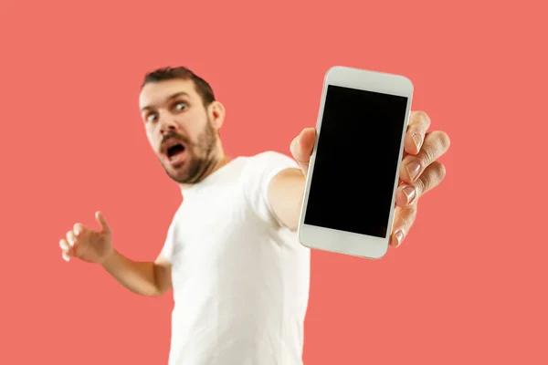 Stock image Young handsome man showing smartphone screen isolated on coral background in shock with a surprise face