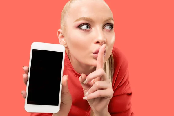 Retrato de una chica casual confiada que muestra el teléfono móvil en blanco aislado sobre el fondo de coral — Foto de Stock