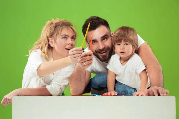 Щаслива сім'я з дитиною разом і посміхається на камеру ізольовані на зеленому — стокове фото
