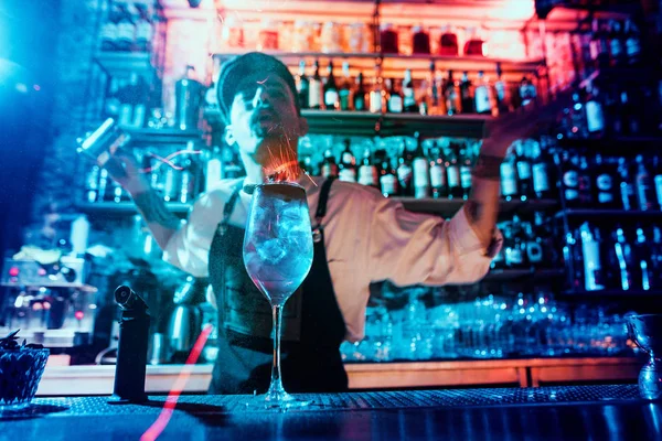 Стакан огненного коктейля на барной стойке на фоне рук барменов с огнем — стоковое фото