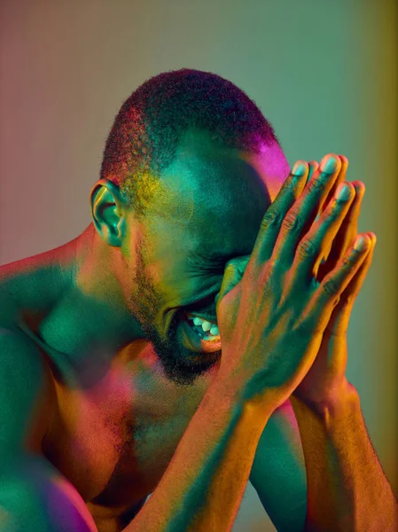 Close up portrait of a young naked african man crying at camera indoors
