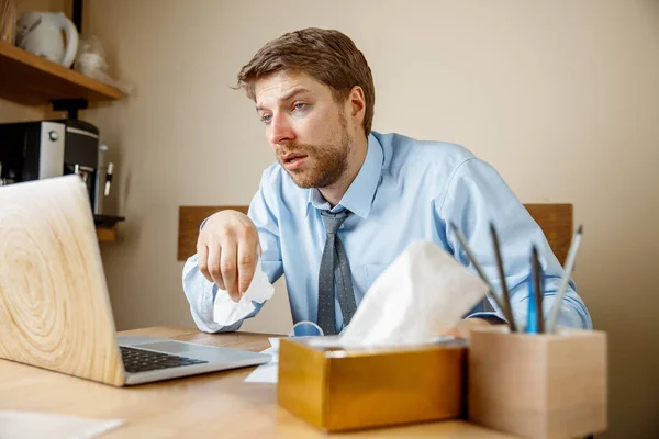 Sick man with handkerchief sneezing blowing nose while working in office, businessman caught cold, seasonal flu. Pandemic influenza, disease prevention, air conditioning in office cause sickness