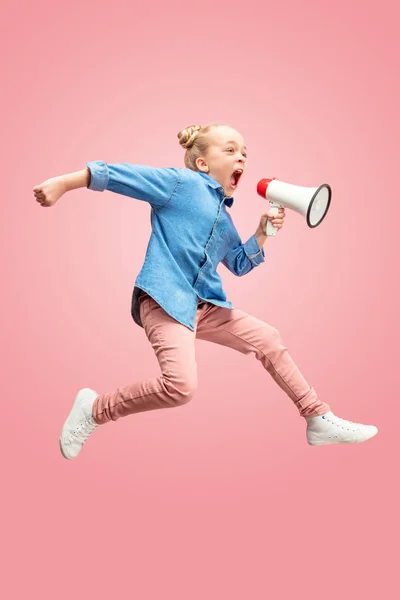 Beautiful young child teen girl jumping with megaphone isolated over pink background