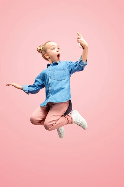 Gelukkig Kaukasische tiener meisje springen met telefoon in de lucht, geïsoleerd op roze studio achtergrond. — Stockfoto