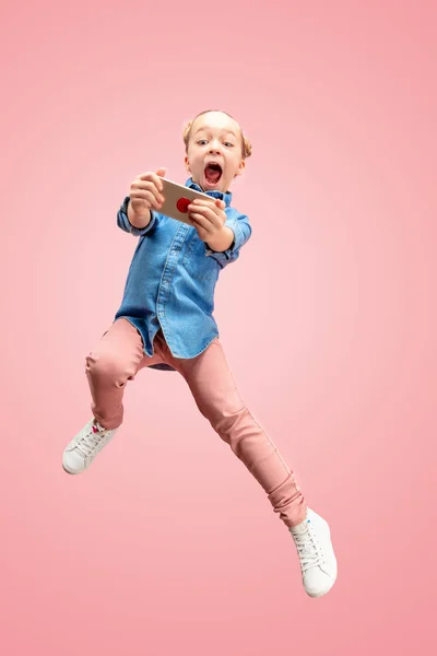 Joven feliz caucásico adolescente chica saltar con el teléfono en el aire, aislado en rosa estudio fondo . — Foto de Stock
