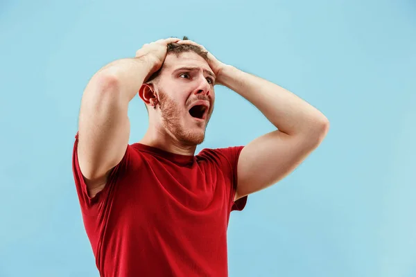 O jovem homem irritado emocional gritando no fundo do estúdio azul — Fotografia de Stock