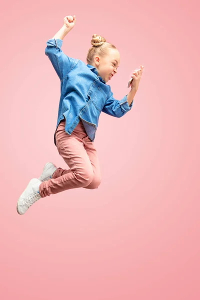 Young happy caucasian teen girl jumping with phone in the air, isolated on pink studio background. — Stock Photo, Image