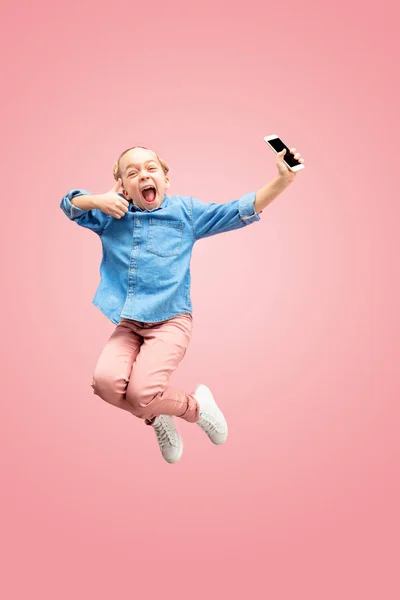 Молода щаслива біла дівчина-підліток стрибає з телефоном в повітрі, ізольована на рожевому студійному фоні . — стокове фото