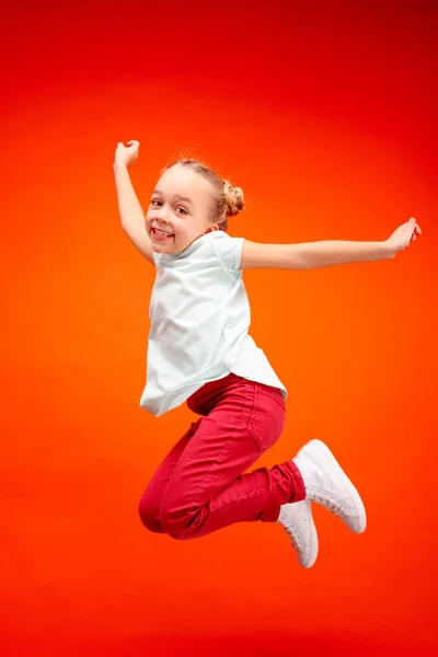 Молода щаслива біла дівчина-підліток стрибає в повітрі, ізольована на червоному студійному фоні . — стокове фото