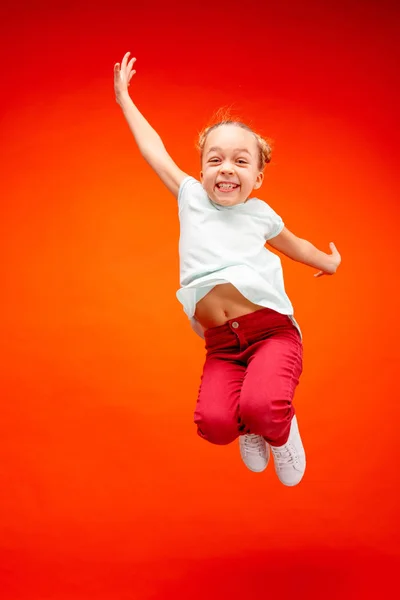 Young happy caucasian teen girl jumping in the air, isolated on red studio background. — Stock Photo, Image