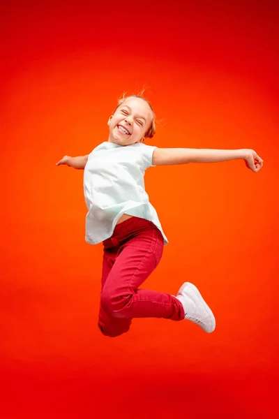 Young happy caucasian teen girl jumping in the air, isolated on red studio background. — Stock Photo, Image