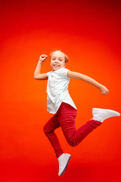 Gelukkig Kaukasische tiener meisje springen in de lucht, geïsoleerd op rode studio achtergrond. — Stockfoto