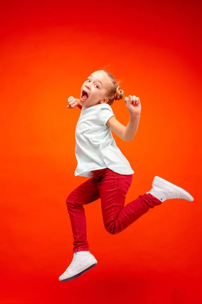 Young happy caucasian teen girl jumping in the air, isolated on red studio background. — Stock Photo, Image
