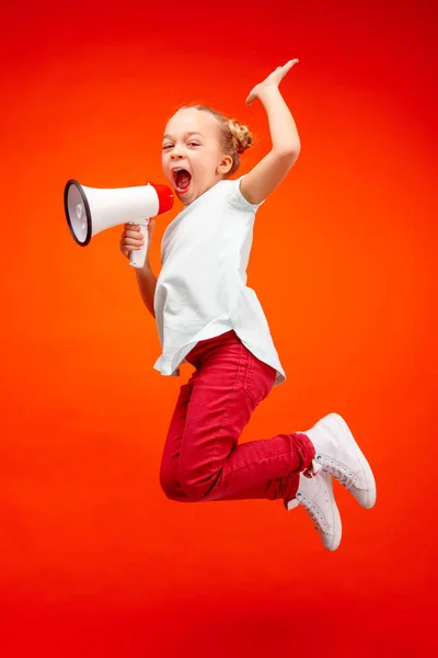 Beautiful young child teen girl jumping with megaphone isolated over red background — Stock Photo, Image