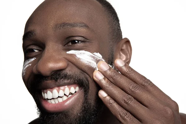 Молодий афро-американський хлопець наносить крем для обличчя під очима на білому тлі — стокове фото