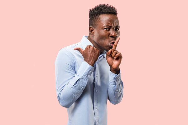 Secret, gossip concept. Young afro man whispering a secret behind his hand. Businessman isolated on trendy pink studio background. Young emotional man. Human emotions, facial expression concept.