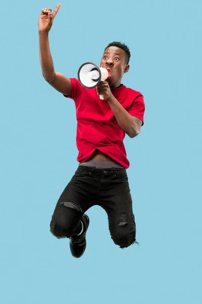 Ventilador de futebol a saltar sobre fundo azul. O jovem afro homem como fã de futebol com megafone — Fotografia de Stock