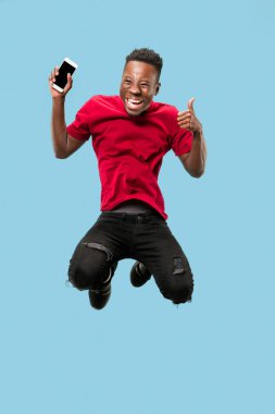 her zaman üstünde hareket eden. Mavi stüdyo arka planı atlama sırasında telefon alarak Afrika yakışıklı genç tam uzunlukta. Mobil, hareket, hareket, iş kavramları