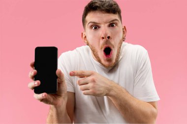 Yakışıklı delikanlı smartphone ekran şok sürpriz yüzü olan pembe arka plan üzerinde izole gösterilen
