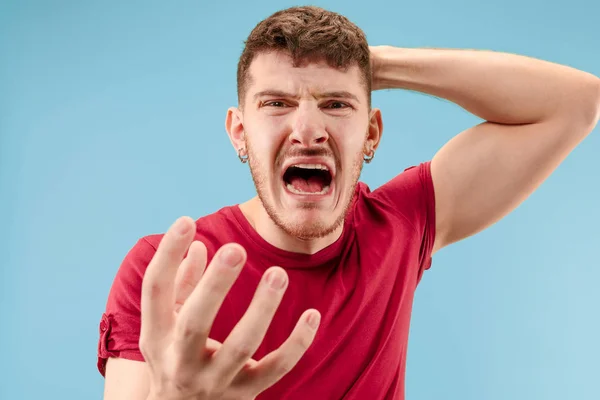 De jonge emotionele boos man schreeuwen op blauwe studio achtergrond — Stockfoto