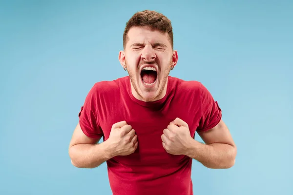 O jovem homem irritado emocional gritando no fundo do estúdio azul — Fotografia de Stock