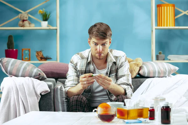Hombre enfermo barbudo con chimenea sentado en el sofá en casa. Enfermedad, gripe, concepto de dolor. Relajación en casa. Conceptos sanitarios . —  Fotos de Stock