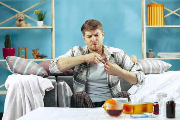 Homme barbu malade avec cheminée assis sur le canapé à la maison. Maladie, grippe, concept de douleur. Détente à la maison. Concepts des soins de santé . — Photo