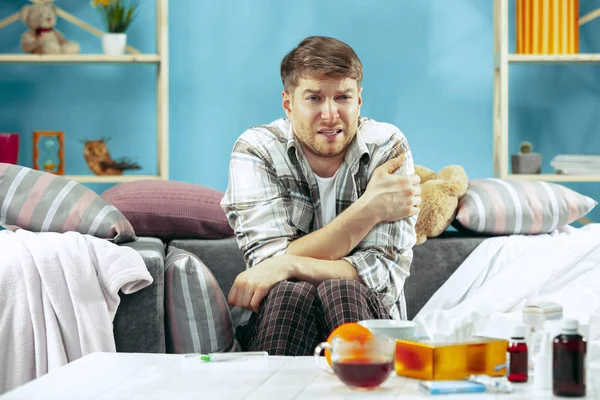 Homme barbu malade avec cheminée assis sur le canapé à la maison. Maladie, grippe, concept de douleur. Détente à la maison. Concepts des soins de santé . — Photo