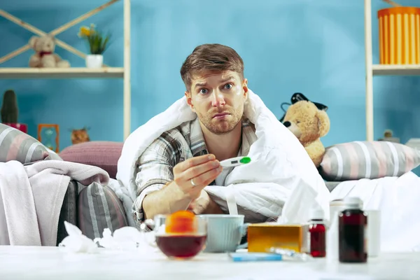 Hombre enfermo barbudo con chimenea sentado en el sofá en casa. Enfermedad, gripe, concepto de dolor. Relajación en casa. Conceptos sanitarios . — Foto de Stock