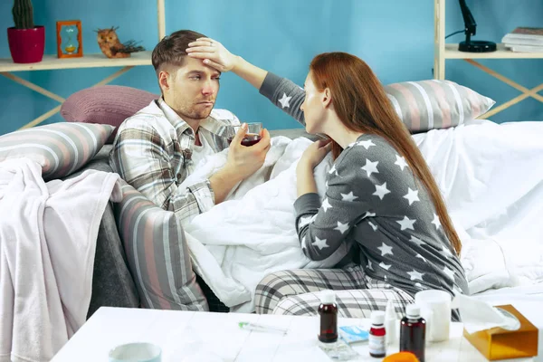Sick man with fever lying in bed having temperature girl take care for him