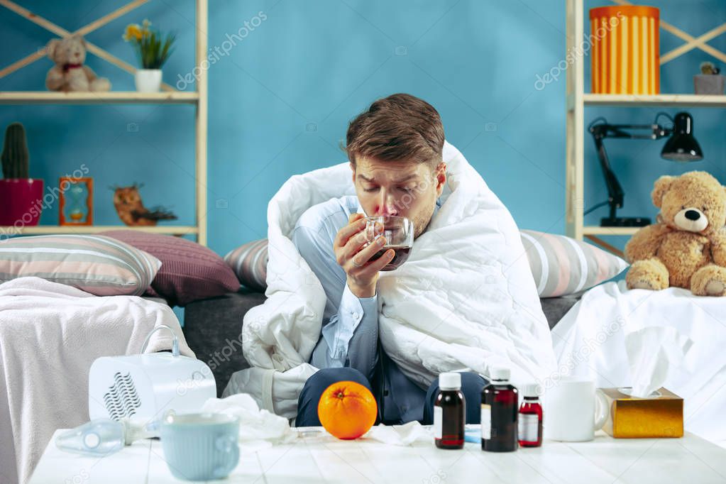 Bearded sick man with flue sitting on sofa at home. Illness, influenza, pain concept. Relaxation at Home. Healthcare Concepts.