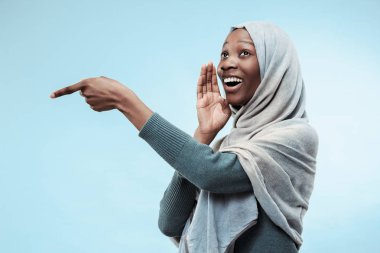 Mavi arka plan üzerinde elini arkasındaki sır fısıldayan genç Afrikalı kadın