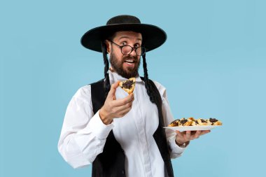 Purim Yahudi festivali için Hamantaschen kurabiyeyle siyah şapkalı genç Ortodoks Yahudi adam