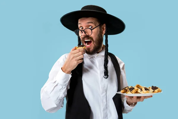 プリムのユダヤ人の祭りの Hamantaschen クッキーと黒い帽子の若い正統派ユダヤ人の男 — ストック写真