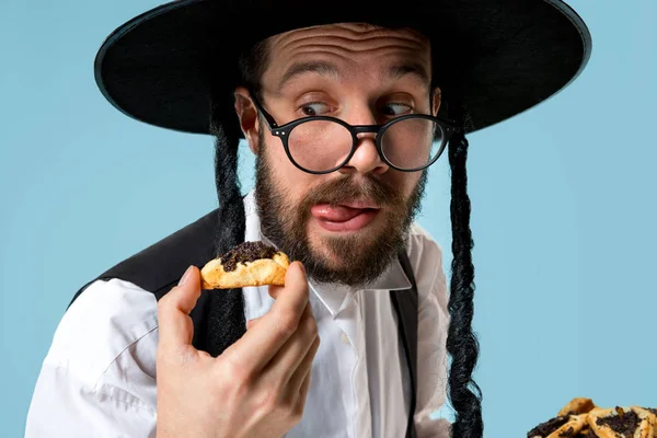 The young orthodox Jewish man with black hat with Hamantaschen cookies for Jewish festival of Purim