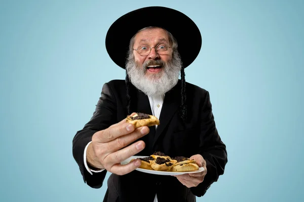 O homem judaico ortodoxo sênior com chapéu preto com biscoitos de Hamantaschen de festival judaico de Purim — Fotografia de Stock