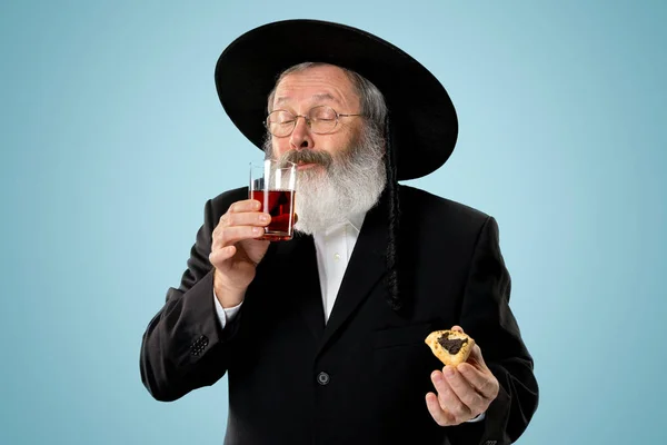 The senior orthodox Jewish man with black hat with Hamantaschen cookies for Jewish festival of Purim