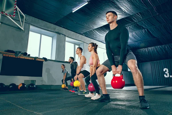 Los jóvenes y fuertes fitness hombres y mujeres en ropa deportiva haciendo ejercicios en el gimnasio —  Fotos de Stock