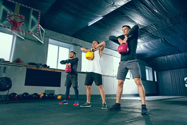Los jóvenes fuertes de fitness en ropa deportiva haciendo ejercicios en el gimnasio —  Fotos de Stock