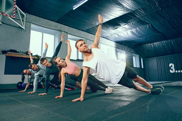 Tiro de hombres jóvenes y una mujer de pie en posición de tabla en el gimnasio —  Fotos de Stock