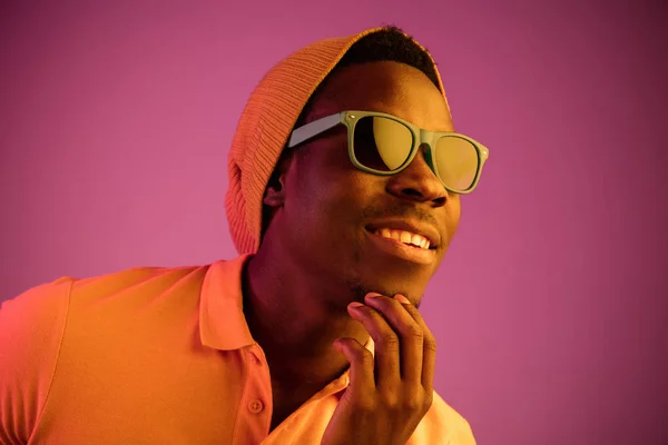Retrato de un joven afroamericano feliz sonriendo sobre fondo de neón negro — Foto de Stock