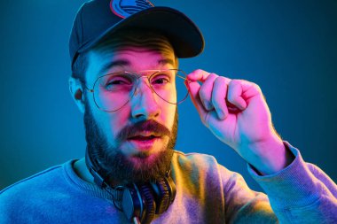 Onun favori müzik keyfi. Korkmuş şık delikanlı müzik duran mavi neon arka plan ses kulaklık ile güneş gözlüğü