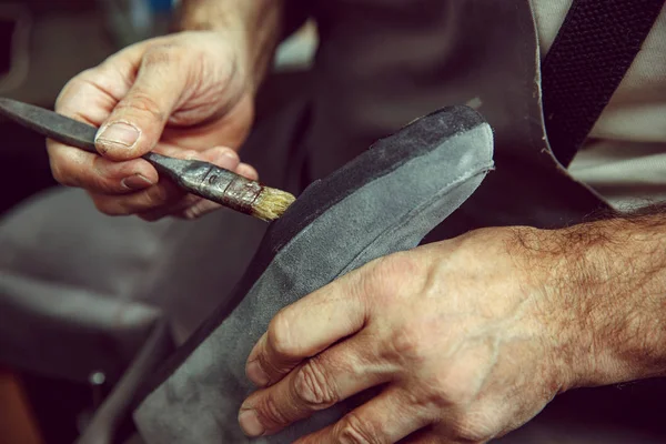 Shoemaker makes shoes for men.He smears special liquid with a brush.