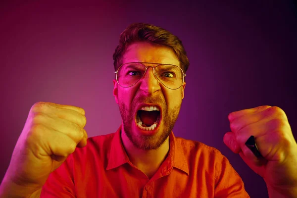 Der junge emotionale wütende Mann schreit auf rosa Studiohintergrund — Stockfoto