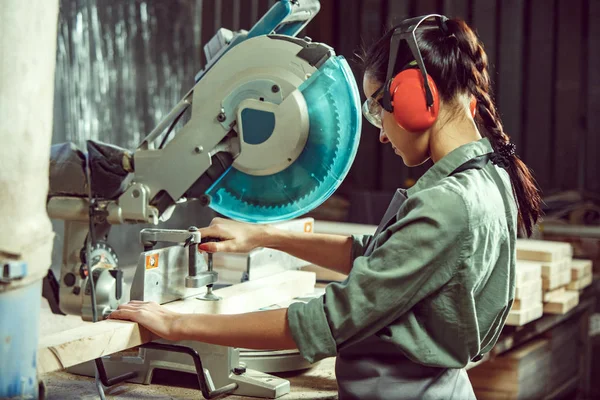 Busy and serious craftswoman grinding timbers with special machine. — Stock Photo, Image