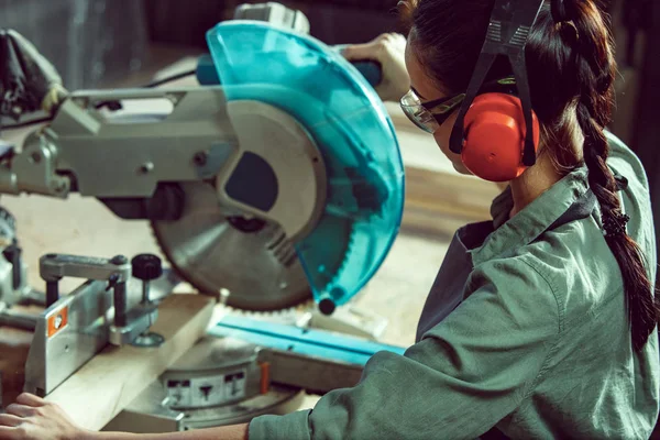 Busy and serious craftswoman grinding timbers with special machine. — Stock Photo, Image