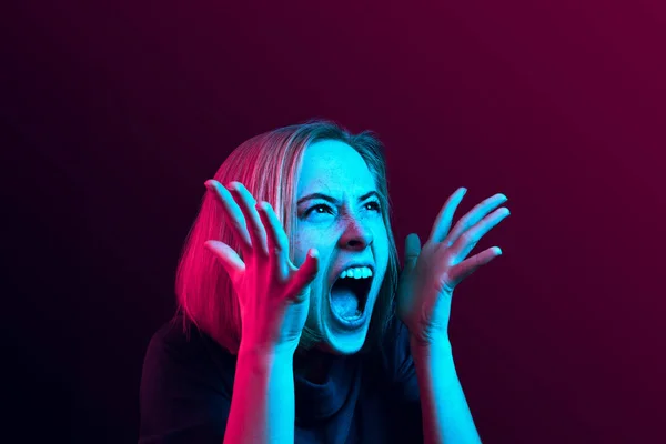 Mladá emocionální naštvaná žena křičí na neon studio pozadí — Stock fotografie
